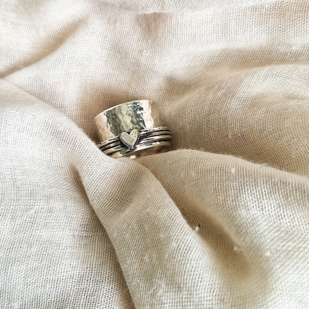 Chunky sterling silver spinner ring with hammered texture and heart embellishment against a white fabric background