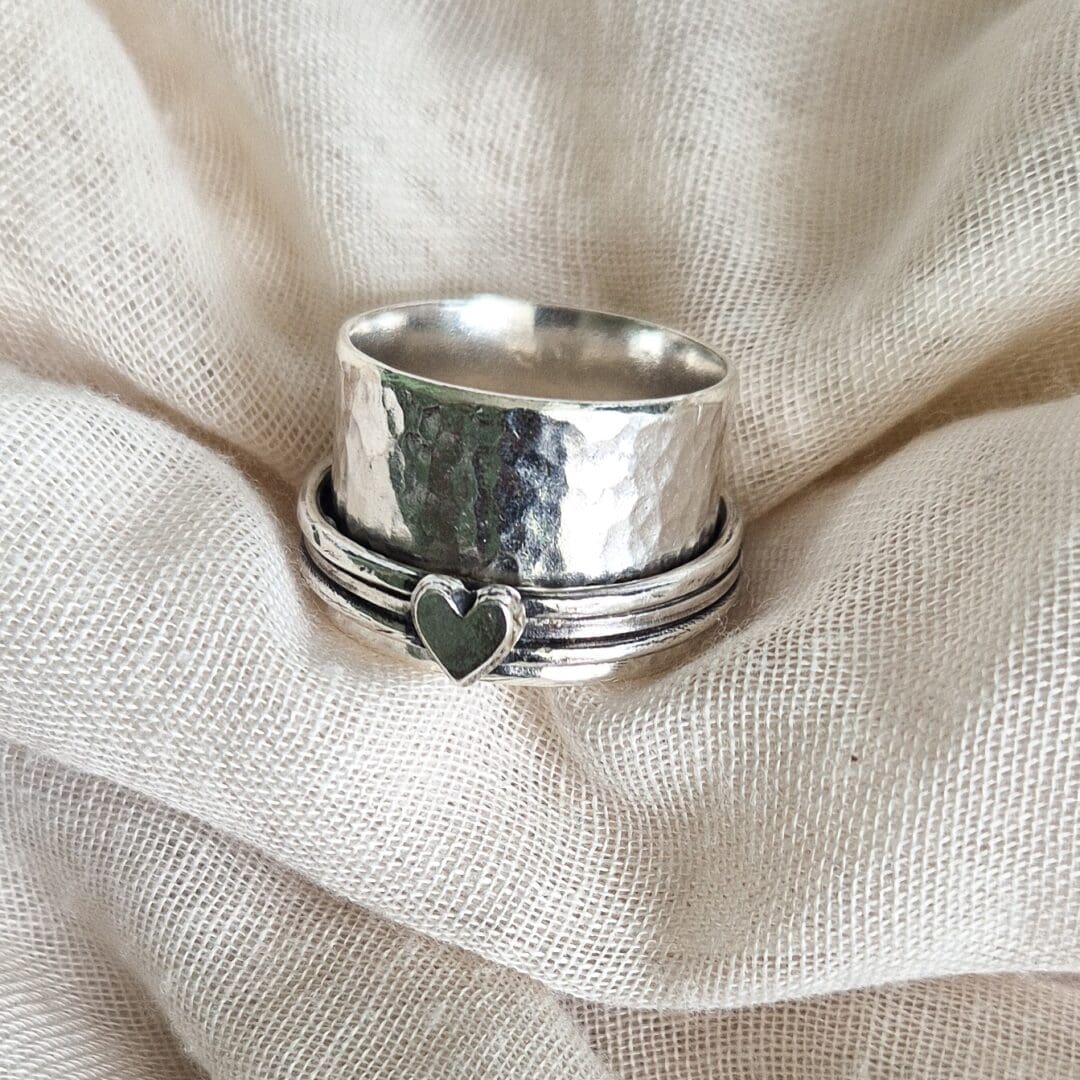 Sterling silver spinner ring with hammered texture and heart embellishment against a white fabric background