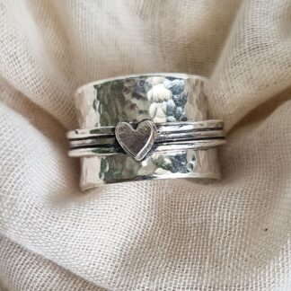 Chunky sterling silver spinner ring with hammered texture and heart embellishment against a white fabric background
