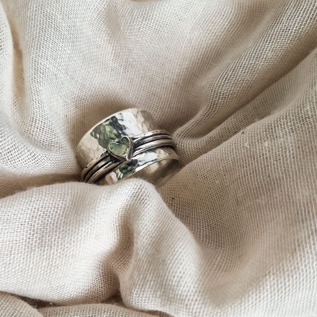 Chunky sterling silver spinner ring with hammered texture and heart embellishment against a white fabric background