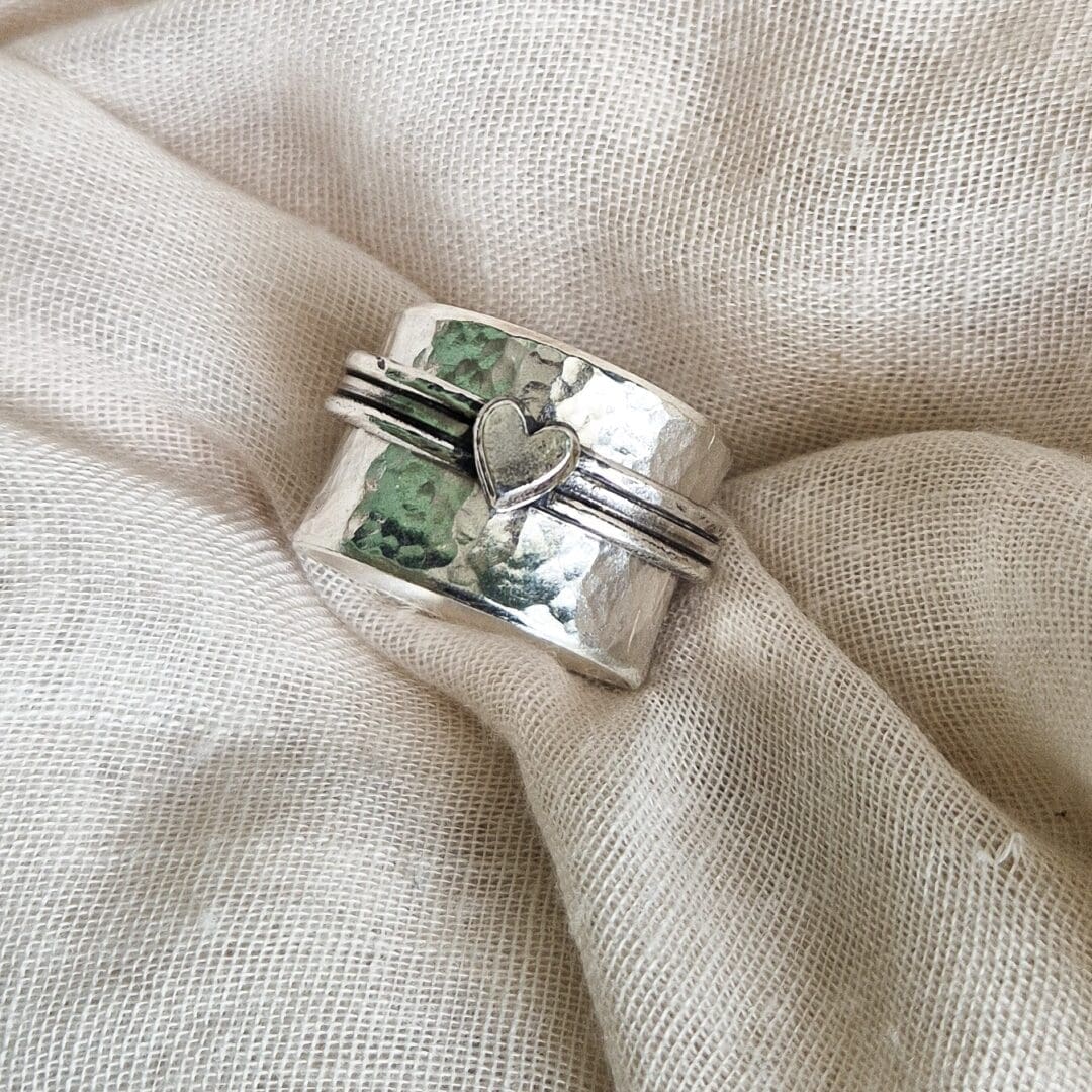 Chunky sterling silver spinner ring with hammered texture and heart embellishment against a white fabric background