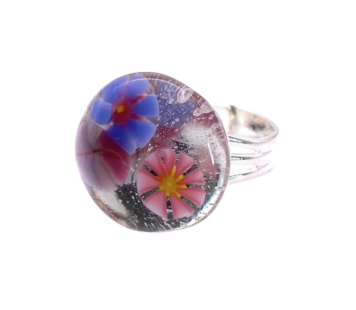 A silver adjustable ring featuring a domed glass top with embedded pink and blue flowers, lilac leaf accents, and small air bubbles for added depth.