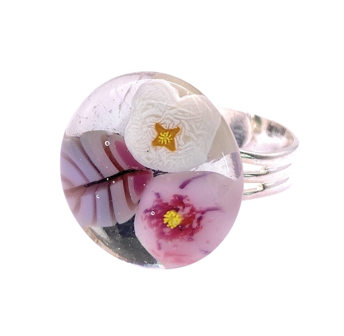 Close-up of a round handmade glass ring featuring pink and white flowers set on a silver band.