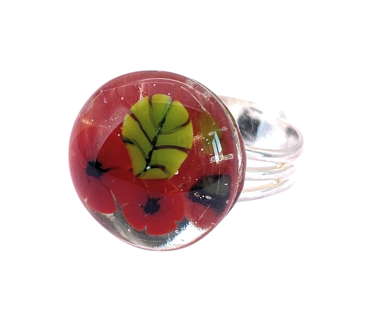 Colorful glass ring featuring red poppies and a green leaf encased in clear glass, set on a silver band.