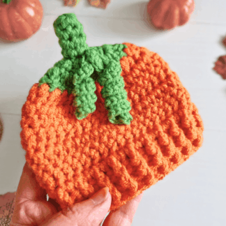 Handmade crochet pumpkin baby hat held showing the curly green stalk, autumn and Halloween gift for newborn to 6 months