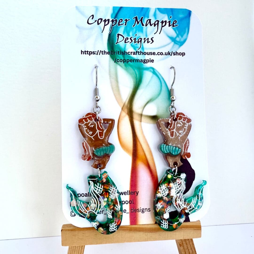 Quirky pin up style mermaids, with red hair and brown tanned skin, green shell bikini and green glitter tail. This two part earrings features a separate toso and tail. They hang off surgical steel ear hooks.