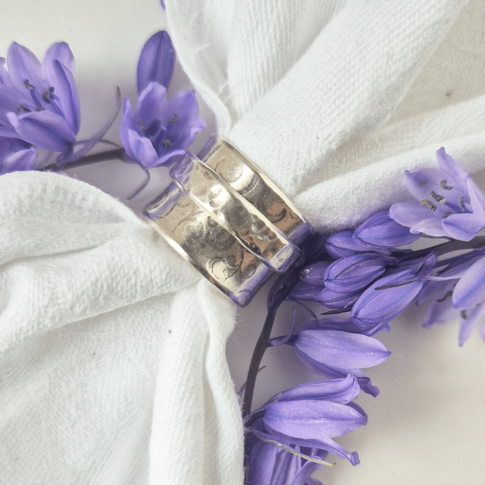 Handcrafted silver spinner ring displayed on white fabric surrounded by blue flowers.