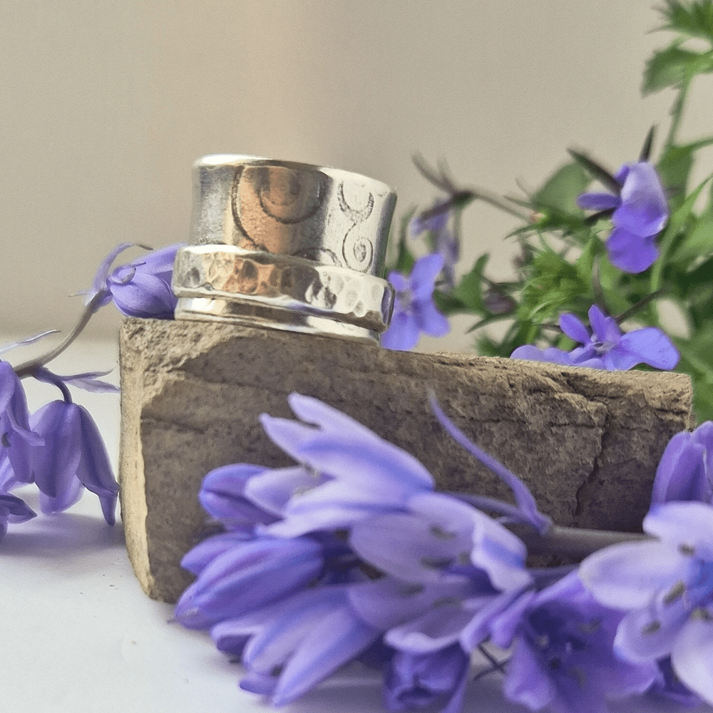 Sterling silver handcrafted spinner ring resting on a rock, surrounded by purple/blue flowers.