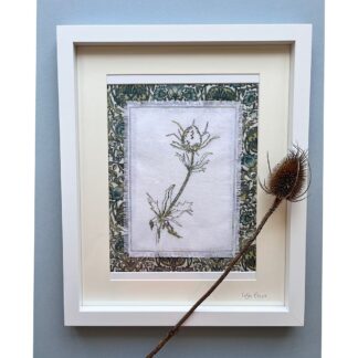 Striking free motion embroidery of a sea holly in green thread on white linen fabric. Mounted on green floral fabric and presented in a white frame