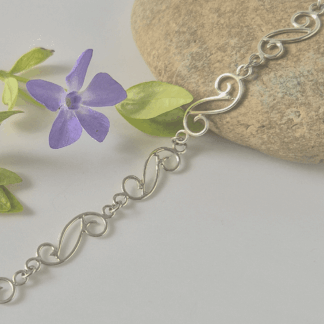 Sterling silver spiral bracelet resting on a stone with a purple flower nearby.