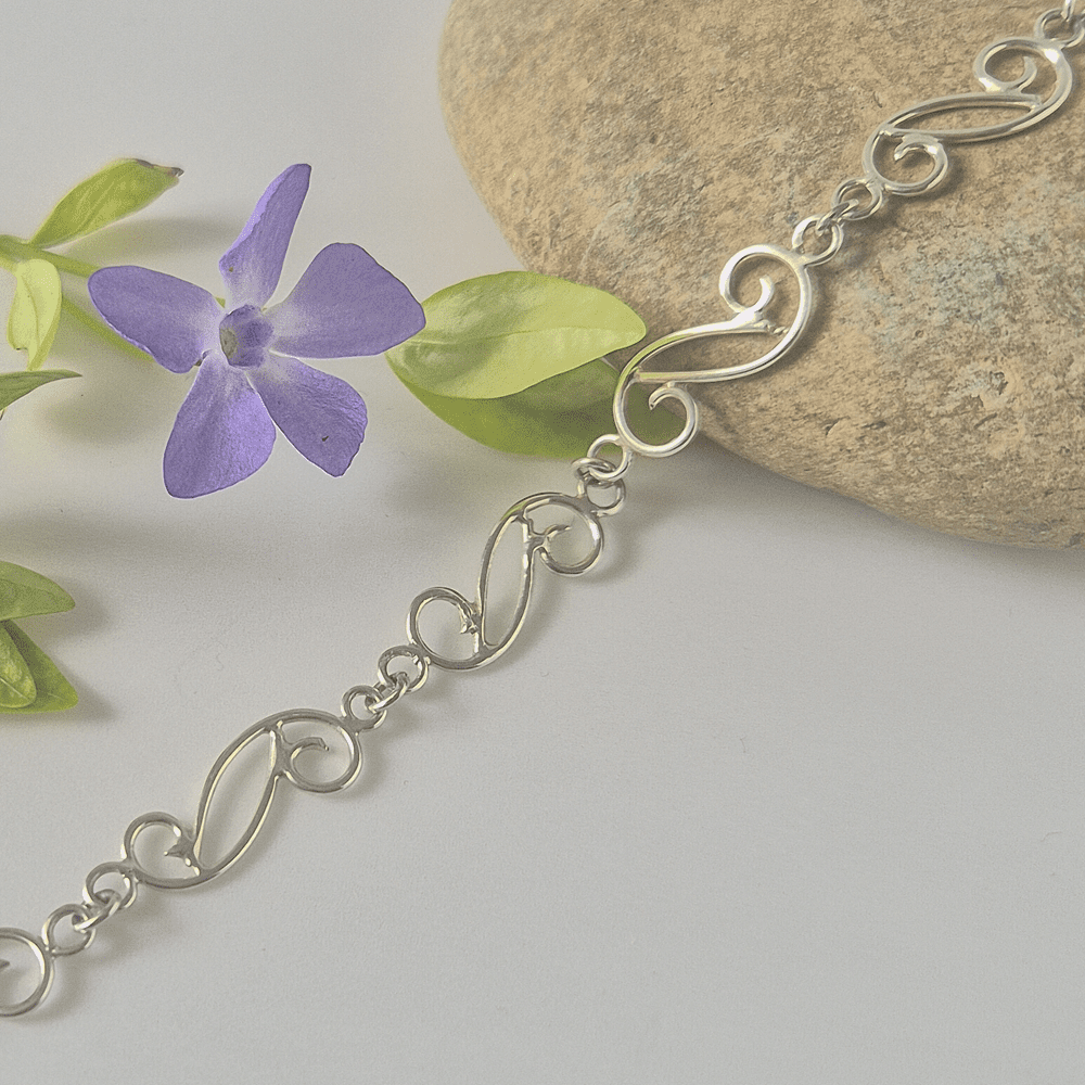 Sterling silver spiral bracelet resting on a stone with a purple flower nearby.