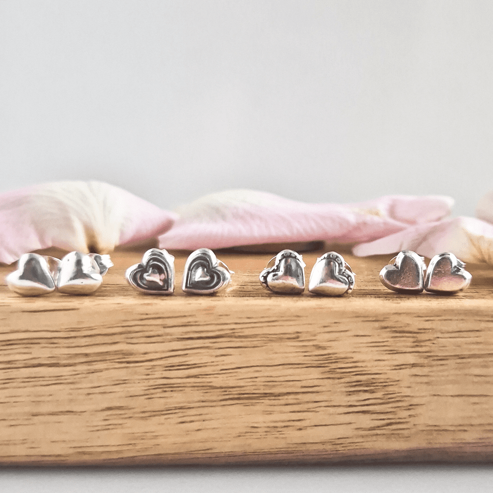 All four styles of studs are lined up next to each other on a piece of wood, with pink petals in the background.