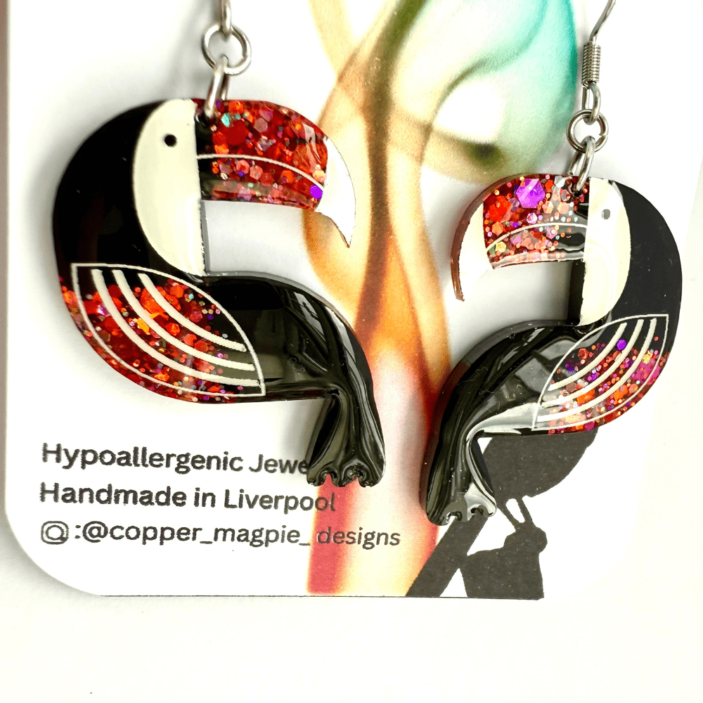 Close-up of toucan earrings showing colourful glitter on the beak and wings.