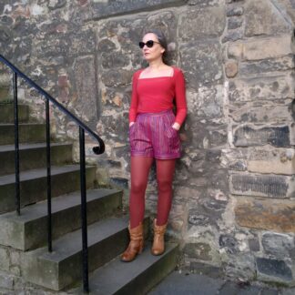 woman wearing purple shorts, orange long sleeve top, browm tights and leather boots