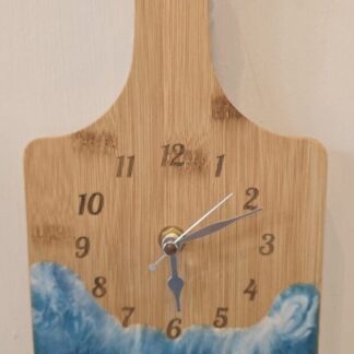 Bamboo chopping board wall clock with engraved numbers and silver hands, featuring a resin wave design in deep blue and white tones.