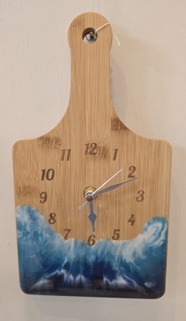 Bamboo chopping board wall clock with engraved numbers and silver hands, featuring a resin wave design in deep blue and white tones.