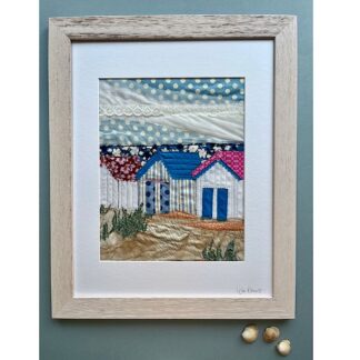 Colourful textile art depicting a row of beach huts appliqued with embroidery detail set against a blue polka dot sky