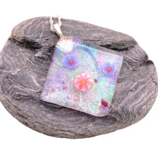 Iridescent glass pendant adorned with pink and blue floral designs, displayed on a textured dark stone background.