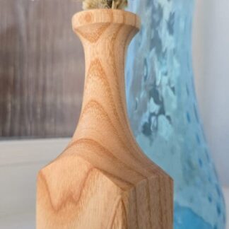 Handmade ash wood bud vase with a tall, elegant neck and square base, holding white and lavender dried flowers, displayed in front of a blue glass vase.