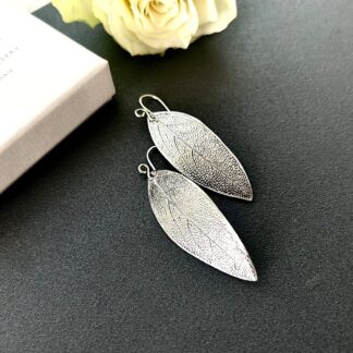 Fine silver clay sage leaf drop earrings with sterling silver ear wires. Displayed on a dark grey tile.