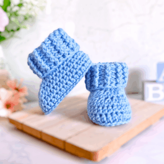 Pair of nigella blue handmade crochet baby booties with a textured ribbed cuff on a neutral background.