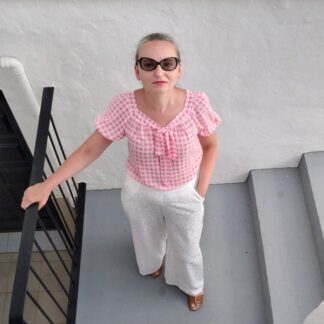 woman wearing pink gingham check blouse and white trousers standing on stairs