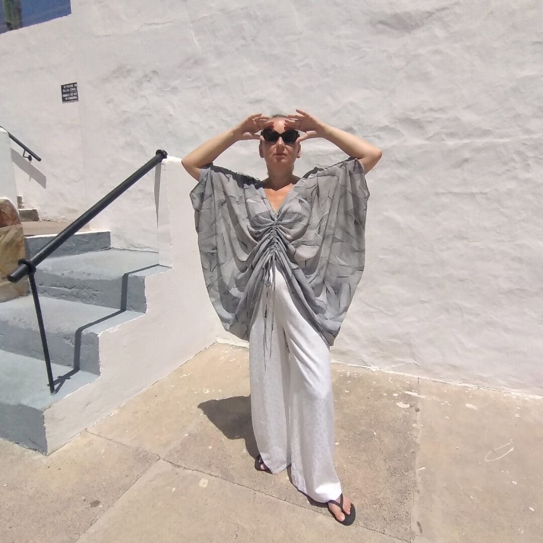 woman wearing draped butterfly shaped top and white wide leg trousers