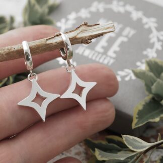 Sterling Silver Four pointed open star leverback hoop earrings shown on hand for scale with Made By Fee Jewellery presentation in background
