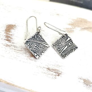 A pair of fine silver handcrafted square drop earrings that have a textured design with sterling silver ear wires. Displayed on white washed wood.