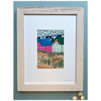 Coastal scene of beach huts in applique set against a blue polka dot sky with grasses and sand dunes in embroidery and fabric.