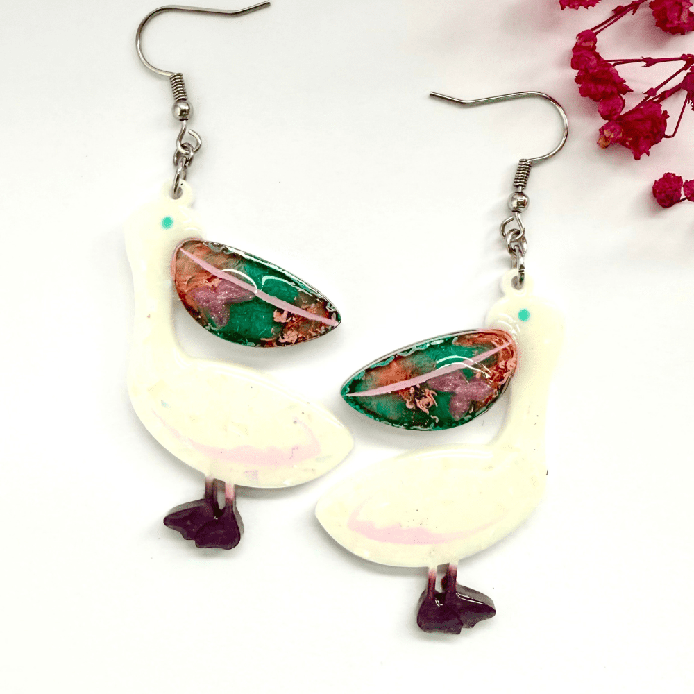 Close-up of resin pelican earrings with pastel bodies and vivid pink/green beaks Handmade bird earrings with whimsical tropical design Lightweight dangle earrings on surgical steel hooks Quirky handmade gift idea for birdwatchers and colour lovers