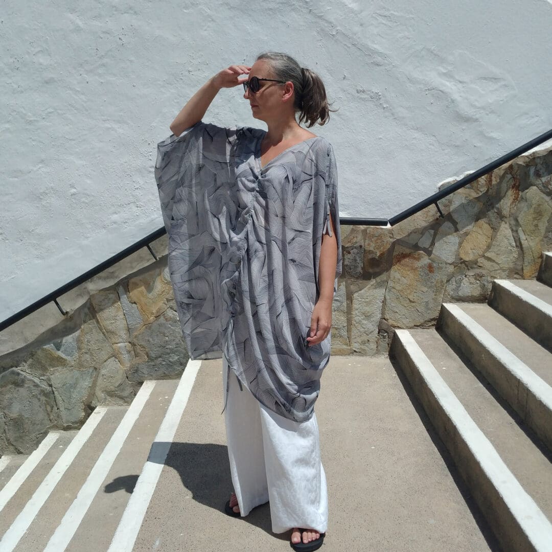 woman wearing drapy beach cover-up in monochrome print and white trousers