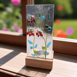 Handmade fused glass candle holder with colourful orchid-inspired flowers, clear glass panel, and wooden base, perfect for windowsill or home décor gift.