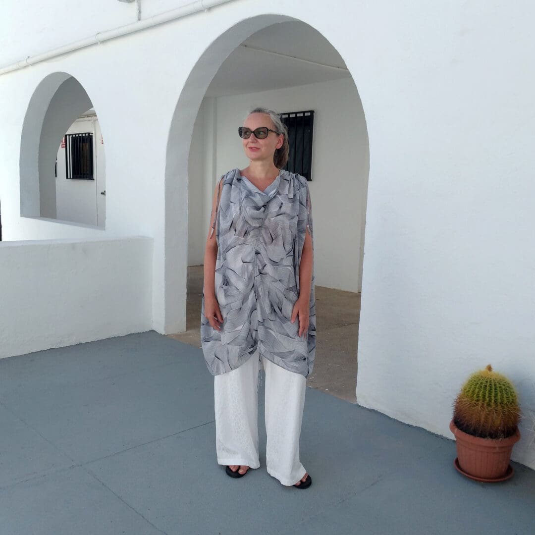 woman dressed in black and white tunic and long white trousers, standing in arched gate