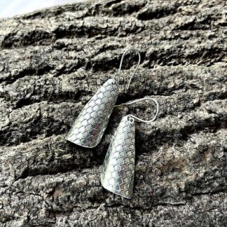 A pair of handmade large fine silver clay drop,earrings with a textured pattern. They have sterling silver ear wires and are displayed on a wood bark background.