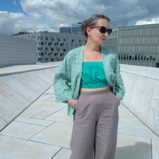 woman in green fluffy bolero top, green strapless bralet and gery linen trousers, walking on the roof of Oslo opera house