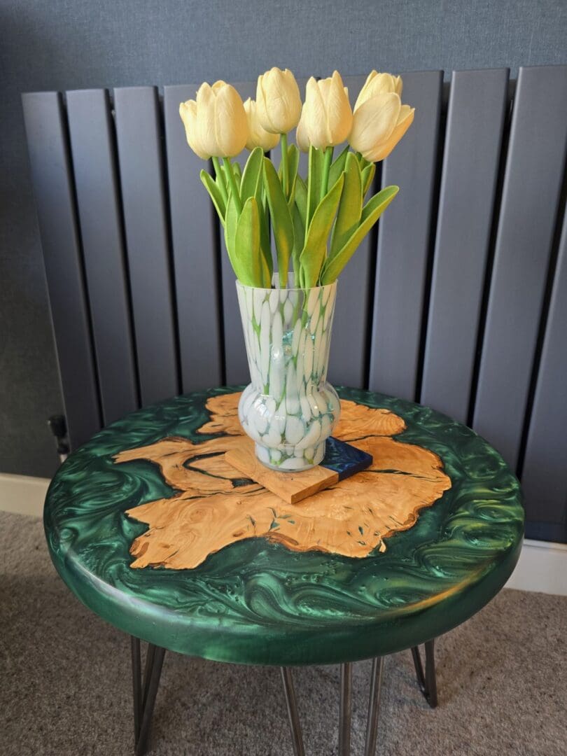 Round olive wood and emerald green resin side table with a vase of cream tulips placed on top.