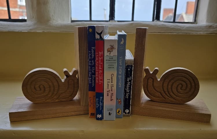 Handmade oak snail bookends holding children’s books, crafted with traditional box joints and finished in natural beeswax.