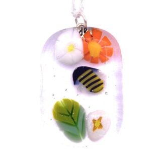 Pendant featuring colorful millefiori glass flowers in white, orange, black, and yellow, with green leaf accents. Encased in clear oval glass, hanging from a silver chain.