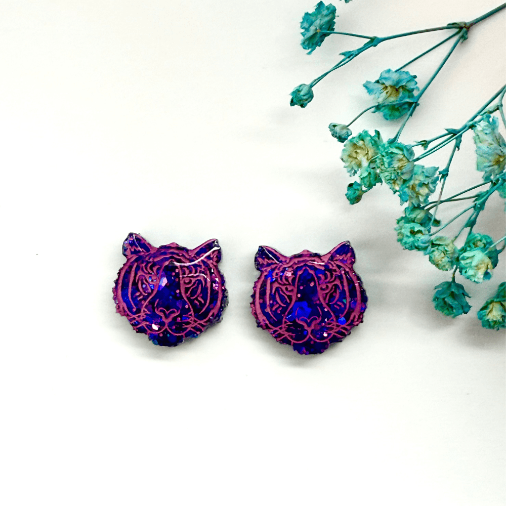 Handmade quirky tiger head earrings displayed flat with flowers”