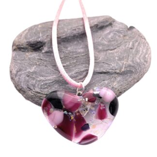 Heart-shaped dichroic glass pendant with pink, purple, and black swirls. It hangs on a pink silk cord over a textured gray stone.