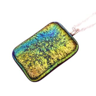 A rectangular, iridescent dichroic glass pendant displays a vibrant mix of blue, green, and gold tones with a textured, crinkled surface. It hangs from a delicate chain.