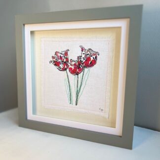 Grey box frame with embroidery of three red fringed tulips standing on a shelf