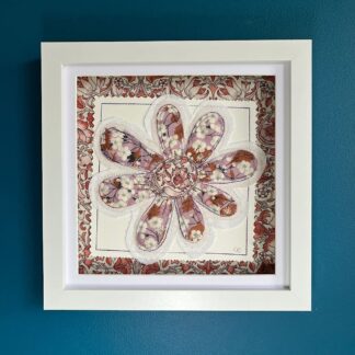 A white box frame on a blue wall, featuring a large single appliqued flower in brown and dusky pink. Mounted on brown floral fabric.