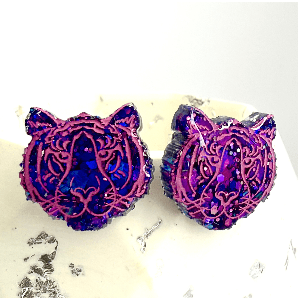 Handmade quirky tiger head earrings displayed on a white and silder background.