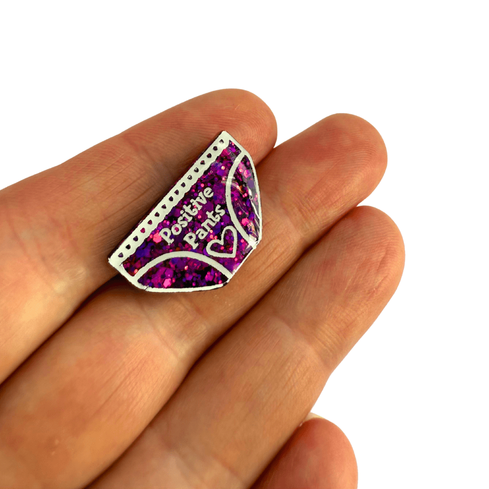 Pink and blue colour-changing resin Positive Pants badge held in hand