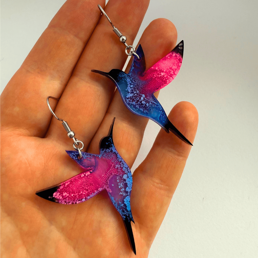 Pair of vibrant hummingbird earrings featuring bold pink and blue alcohol ink resin