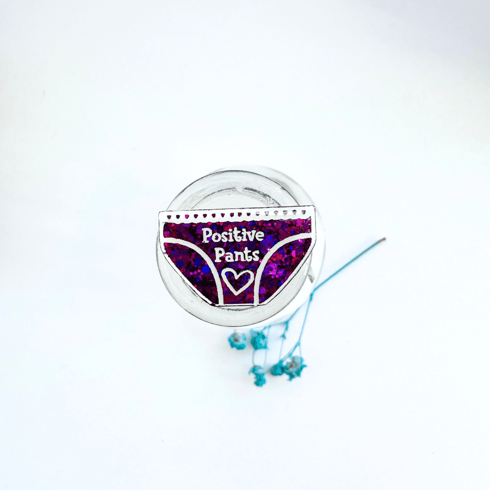 Close-up of handmade pink and blue colourshift Positive Pants Pin Badge in epoxy resin