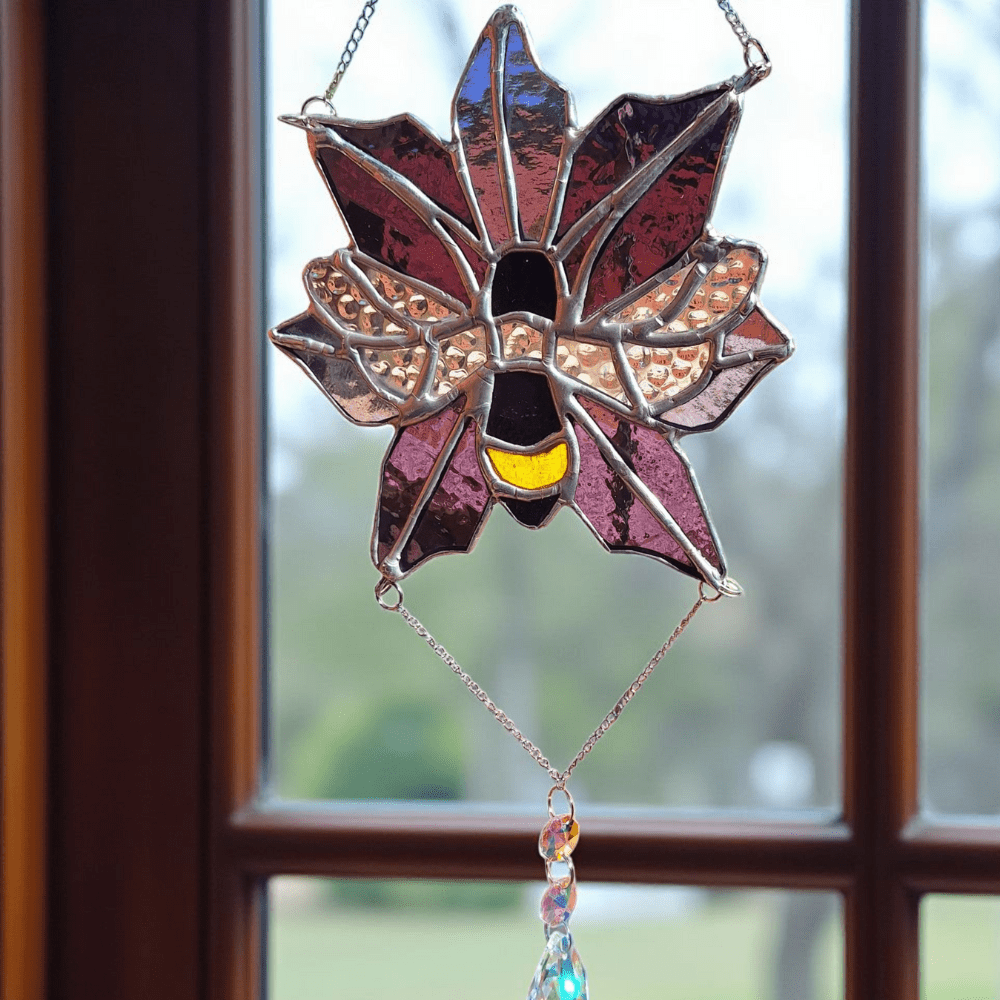 Handmade stained glass flower suncatcher with a bee in the centre and a crystal teardrop, hanging in a window with sunlight