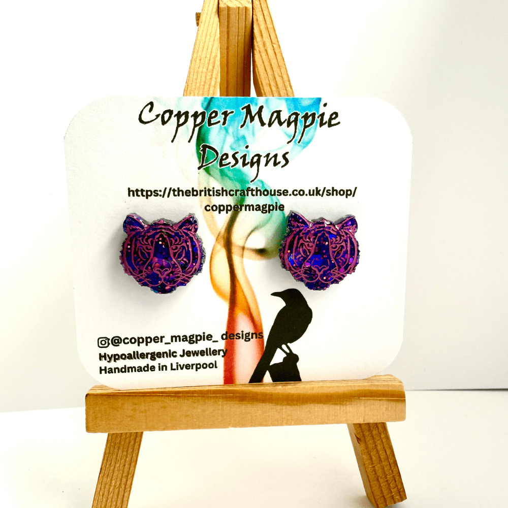 Purple and pink glitter tiger head earrings for animal lovers on a branded card for Copper Magpie Designs, resting on a minature easel